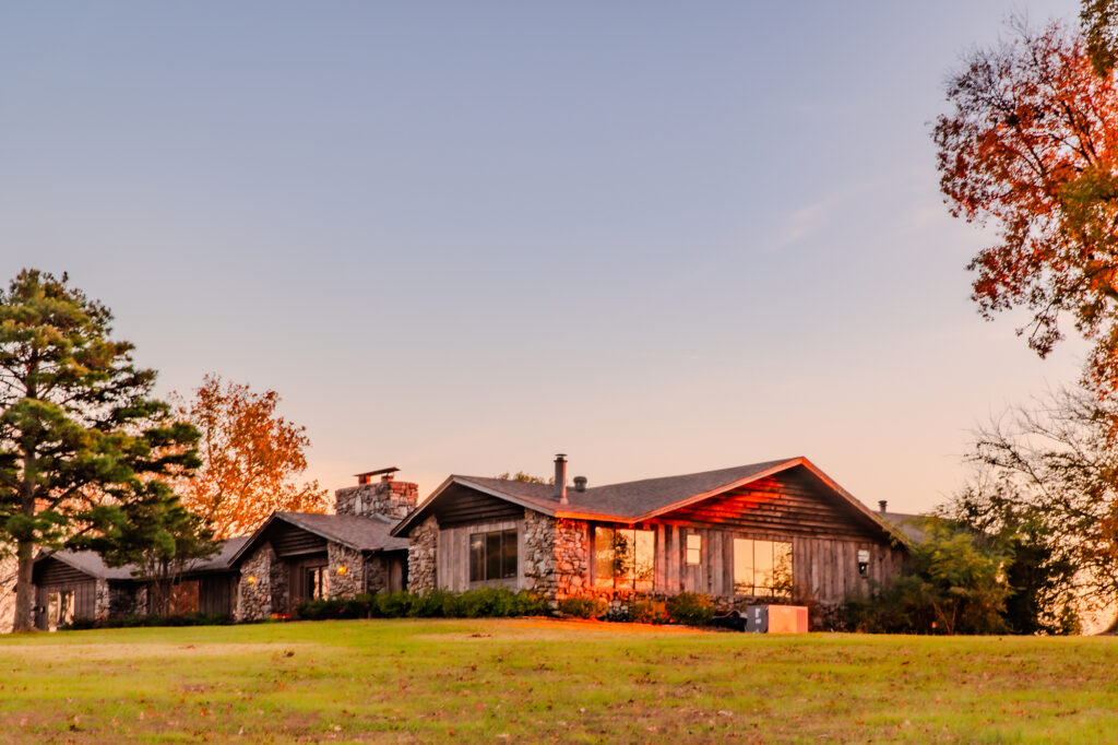 The Lodge at Peaceful Pointe, a rustic stone and wood venue surrounded by trees and open grass, illuminated by the warm glow of sunset.